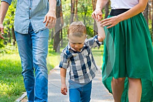 Dad and mom hold their son by the hand and walk along the park r