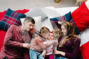 The dad, mom hug little son and daughter on bed in bedroom. Happy New Year and Merry Christmas. Top view, flatlay. The