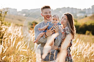 Dad, mom hugging daughter outdoors in grass on sunset. The concept of summer holiday. Mother`s, father`s, baby`s day. Family