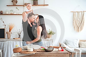 Relationship in the family with small children. Dad and mom kiss in the bright kitchen, children help to cook in the kitchen