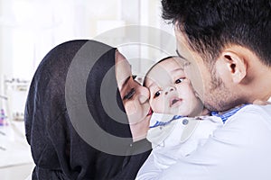 Dad and mom kissing baby cheeks