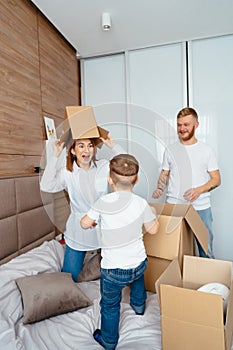 Dad mom and little son play in the bedroom with paper boxes