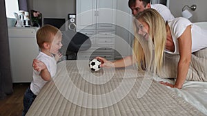 Dad and mom play with the boy on the bed with the ball