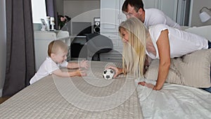 Dad and mom play with the boy on the bed with the ball