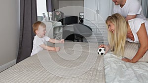 Dad and mom play with the boy on the bed with the ball