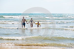 Dad, mom and son come out of the sea after swimming. Bif storm waves. Boy iin water wings.