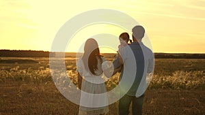 Dad and mother with their beloved daughter in their arms walk in the park at sunset. Happy child plays with father and