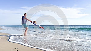 Dad play with daughter girl on the beach spin holding hands