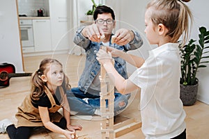 Dad and children playing building high tower from wooden blocks