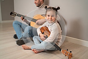 Dad plays the guitar with his daughter. The child learns to play a musical instrument with a tutor. Musical duet of a