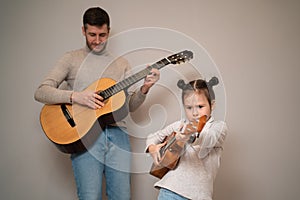 Dad plays the guitar with his daughter. The child learns to play a musical instrument with a tutor. Musical duet of a