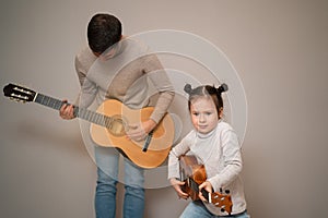 Dad plays the guitar with his daughter. The child learns to play a musical instrument with a tutor. Musical duet of a