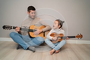 Dad plays the guitar with his daughter. The child learns to play a musical instrument with a tutor. Musical duet of a