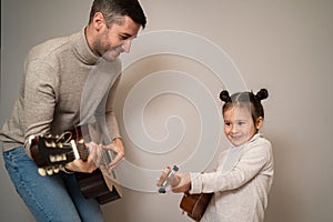 Dad plays the guitar with his daughter. The child learns to play a musical instrument with a tutor. Musical duet of a