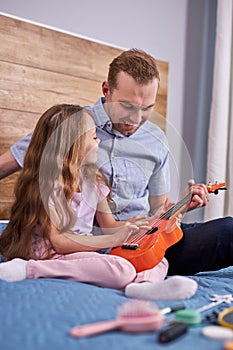 Dad plays guitar with his daughter. little child learns to play musical instrument with tutor