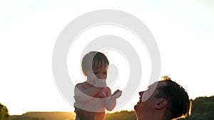 Dad plays with little baby in highlights of sunset on beach during high summer season. Parent throws child up and laughs