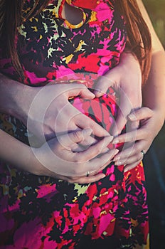 Dad's and mom's hands in heart shape on the belly of the future baby