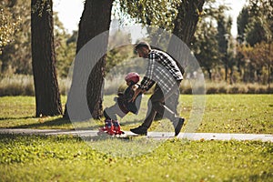 Dad saves his daughter from falling on roller skates in the park. Paternal support and care. Film grain photo