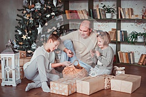 Dad, son and daughter sitting at the Christmas tree. Warm colour. They `re watching a basket of cones