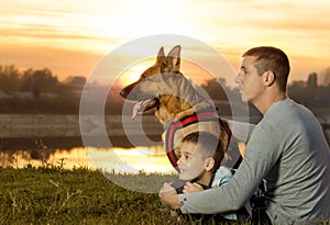 Dad and son and German shepherd in nature watching the sunset