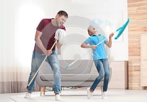 Dad and son having fun while cleaning living room