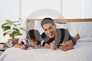 Dad and son having goodtime playing vdo game together on bed at home