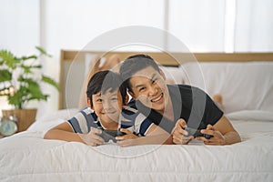 Dad and son having goodtime playing vdo game together on bed at home