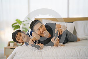 Dad and son having goodtime playing vdo game together on bed at home photo