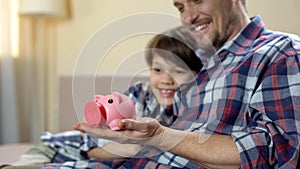 Dad and son holding piggy-bank and smiling, social welfare, health insurance