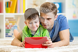 Dad and son kid play with tablet computer indoors