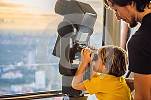 Dad and son are looking at Kuala lumpur cityscape. Use binoculars. Panoramic view of Kuala Lumpur city skyline evening