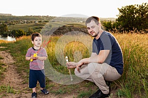 Dad and son play fun soap bubbles in nature in a yellow summer field. Hanging with his father, fatherhood and childhood. Father`s