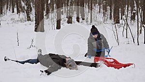 Dad and son are playing in winter snowy forest. Man lies in snow, makes angel.