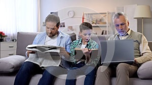 Dad and son reading book and newspaper, aging man holding laptop, generations