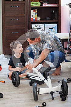 Dad and son are repairing a four-wheeled bicycle, a man shows a child how to drill, they smile and have fun while repairing