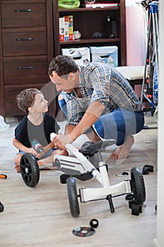 Dad and son are repairing a four-wheeled bicycle, a man shows a child how to drill, they smile and have fun while repairing