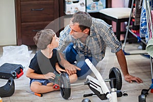 Dad and son are repairing a four-wheeled bicycle, a man shows a child how to drill, they smile and have fun while repairing