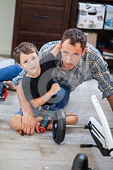 Dad and son are repairing a four-wheeled bicycle, a man shows a child how to drill, they smile and have fun while repairing