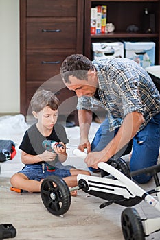 Dad and son are repairing a four-wheeled bicycle, a man shows a child how to drill, they smile and have fun while repairing