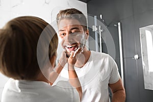 Dad and son with shaving foam on faces having fun in bathroom