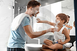 Dad and son with shaving foam on faces having fun in bathroom