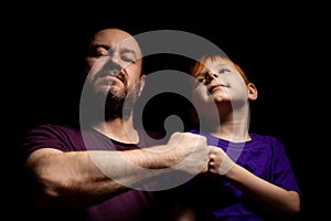 Dad and son are smiling and banging their fists against each other on a black background. Parent-child interaction. Father`s day