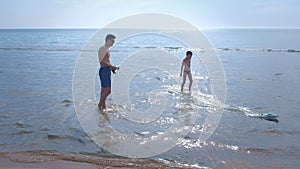 Dad and son start the toy motor boat at the sea beach.