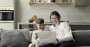 Dad son teenager cuddle on couch focused on laptop screen