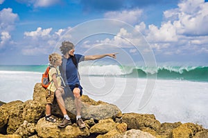 Dad and son travelers on amazing Melasti Beach with turquoise water, Bali Island Indonesia. Traveling with kids concept