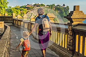 Dad and son travelers in Pura Luhur Uluwatu temple, Bali, Indonesia. Amazing landscape - cliff with blue sky and sea. Traveling wi