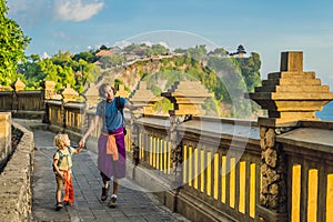 Dad and son travelers in Pura Luhur Uluwatu temple, Bali, Indonesia. Amazing landscape - cliff with blue sky and sea. Traveling wi