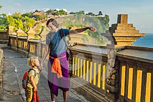 Dad and son travelers in Pura Luhur Uluwatu temple, Bali, Indonesia. Amazing landscape - cliff with blue sky and sea. Traveling wi