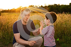 Dad and son walk in a yellow summer field in the evening at sunset and eat candy on a stick. Father`s Day, love in the family, th