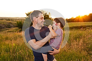 Dad and son walk in a yellow summer field in the evening at sunset and eat candy on a stick. Father`s Day, love in the family, th